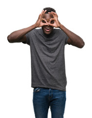 Fototapeta premium Young african american man wearing grey t-shirt doing ok gesture like binoculars sticking tongue out, eyes looking through fingers. Crazy expression.