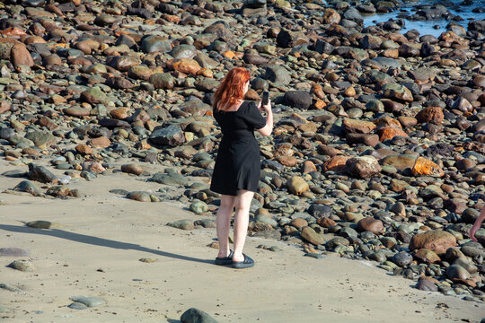 Young woman  stands on a stony beach and takes photos with her cell phone