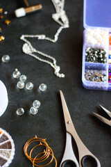 Box with colorful beads, string, wire, chain, scissors, pliers and hammer on dark background. Various jewelry making supplies. Selective focus.