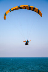 Paraglider flying over the sea coast in blue sky background