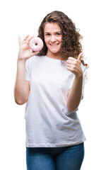 Young brunette girl eating donut over isolated background happy with big smile doing ok sign, thumb...