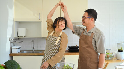Shot of happy middle aged couple dancing together while preparing healthy dinner in the kitchen.