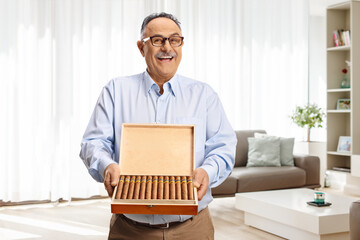 Mature man with a box of cuban cigars standing in a living room