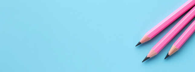 Three pink pencils on light blue background. Top view, copy space for text. Education, drawing, back to school background
