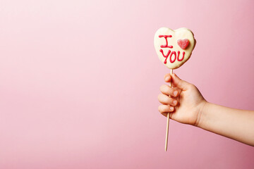Child hand holding Valentine's day heart shape candy with white chocolate on pastel pink background. Love Concept