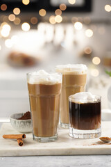Three tall glasses with warm coffee drink with cinnamon, whipped milk foam and caramel on a marble board with bokeh fairy lights in the background