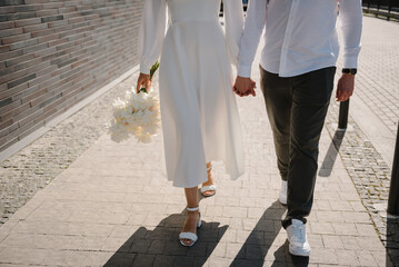 The bride and groom with a wedding bouquet, holding hands and walking on the road on the street....