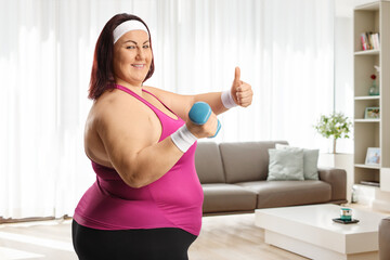 Corpulent woman holding dumbbell and gesturing thumbs up