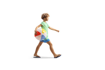 Full length profile shot of a boy walking and carrying a beach ball