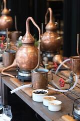 Small copper stills and distilling equipment arranged on a decorated table.
