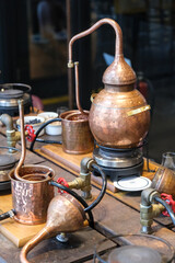 Small copper stills and distilling equipment arranged on a decorated table.