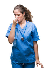 Young brunette doctor girl wearing nurse or surgeon uniform over isolated background smelling...