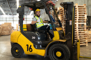 Warehouse worker wears safety helmet driving forklift truck in pallet factory. Skilled male logistic engineer working in shipping storage manufacturing lifting, moving and unloading cargo for delivery