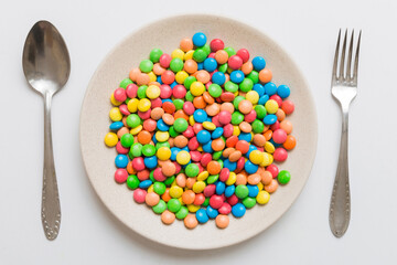 cutlery on table and sweet plate of candy. Health and obesity concept, top view on colored background