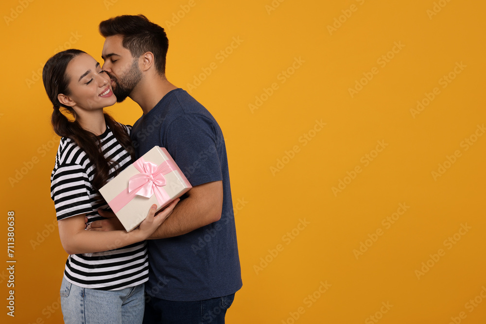 Poster Man kissing his smiling girlfriend on orange background, space for text. Celebrating holiday