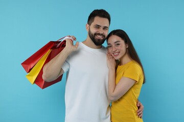 Happy couple with shopping bags on light blue background