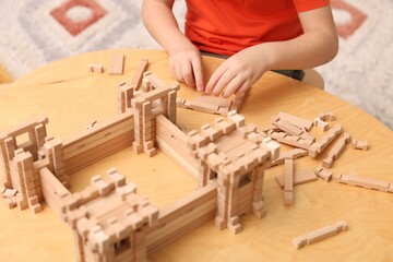 Little boy playing with wooden construction set at table in room, closeup. Child's toy