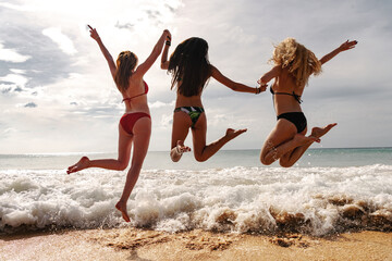 Three happy young girls are having fun and jumps at sea beach