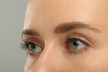 Fototapeta premium Woman with long eyelashes after mascara applying against grey background, closeup