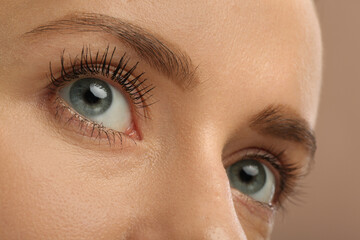 Woman showing difference in eyelashes length after mascara applying against light brown, closeup