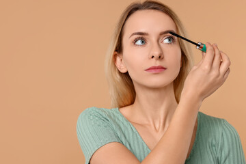 Beautiful woman applying mascara on beige background. Space for text