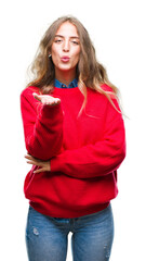 Beautiful young blonde woman wearing winter sweater over isolated background looking at the camera blowing a kiss with hand on air being lovely and sexy. Love expression.