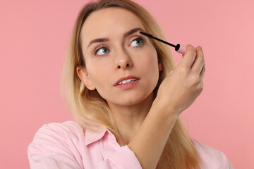 Beautiful woman applying mascara on pink background, closeup