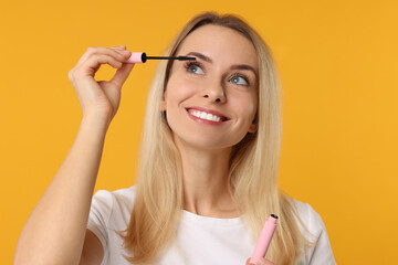 Beautiful woman applying mascara on orange background
