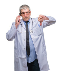 Handsome senior doctor man talking on smarpthone over isolated background with angry face, negative sign showing dislike with thumbs down, rejection concept