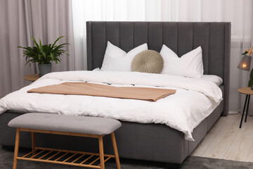 Stylish bedroom interior with large bed, ottoman, lamp and houseplant