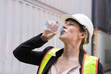 Female container worker drinking water in break time at commercial dock site
