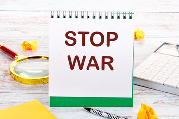 STOP WAR text on the white sheet of the notebook is next to a magnifying glass, calculator, pencil, stickers