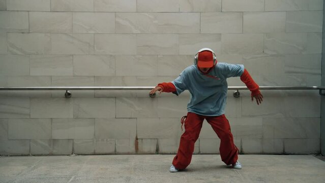 Handsome choreographer practice street dance in gray background. Young attractive b boy dancer perform while wearing stylish cloth. Feeling of lively step. Copy space. Outdoor sport 2024. Sprightly.