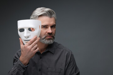 Multiple personality concept. Man with mask on dark grey background, space for text
