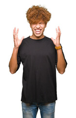 Young handsome man with afro hair wearing black t-shirt crazy and mad shouting and yelling with aggressive expression and arms raised. Frustration concept.