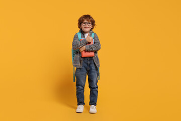 Fototapeta premium Happy schoolboy with backpack and books on orange background