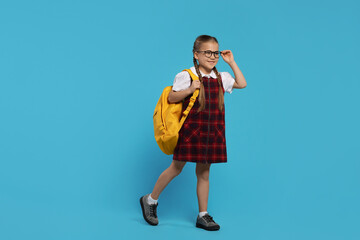 Happy schoolgirl in glasses with backpack on light blue background