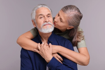 Senior woman kissing her beloved man on light grey background