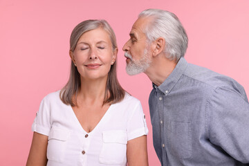 Senior man kissing his beloved woman on pink background