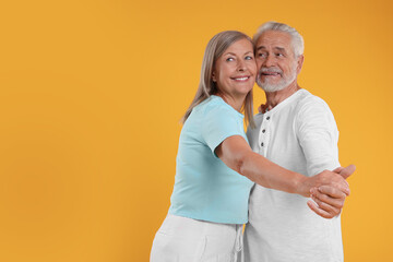 Senior couple dancing together on orange background, space for text