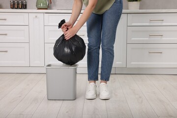 Woman taking garbage bag out of trash bin in kitchen, closeup