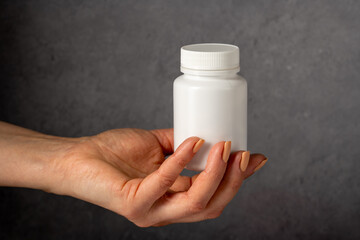 Female hand holding a white plastic bottle with pills. Capsules, collagen, vitamins, pain killers or drugs