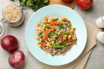Tasty pearl barley porridge with vegetables on light textured table, flat lay