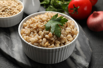 Tasty pearl barley porridge and parsley in bowl on dark textured table, closeup
