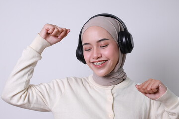 Young smiling Asian muslim woman with braces and hijab using headphones listen to music isolated on white background