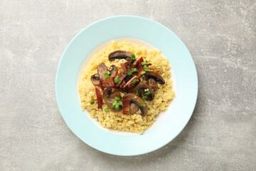 Tasty millet porridge with mushrooms, bacon and green onion on grey textured table, top view