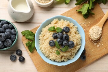 Tasty quinoa porridge with blueberries and mint in bowl on light wooden table, flat lay