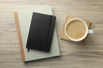 Different notebooks and cup of coffee on wooden table, flat lay