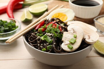 Tasty buckwheat noodles (soba) with mushrooms, onion, chili pepper, egg and chopsticks on wooden table, closeup