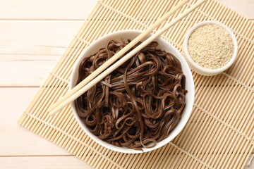 Tasty buckwheat noodles (soba) with sesame and chopsticks on wooden table, flat lay